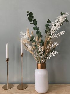 two candles are next to a vase with flowers and greenery in it on a wooden table