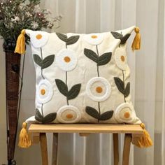 a white pillow with yellow tassels sitting on a wooden chair next to a vase