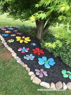 a garden path made out of rocks and stones with colorful flowers on the ground next to a tree