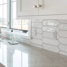 a kitchen with white cabinets and marble counter tops in front of a window that is open