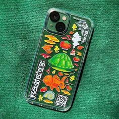 an iphone case with stickers on it sitting on a green towel next to a cell phone