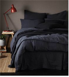 a bed with dark blue linens and a red lamp on the nightstand next to it