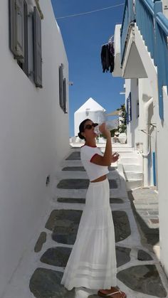 a woman in a white dress is drinking from a bottle while walking down the street