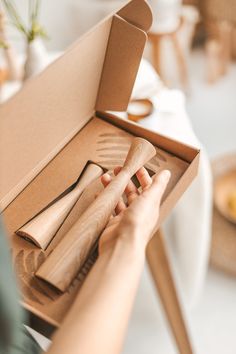 a person holding a wooden spoon and fork in a box on a table with other items