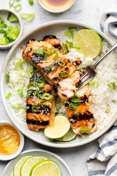 a white plate topped with chicken and rice next to limes, lemon wedges and sauce