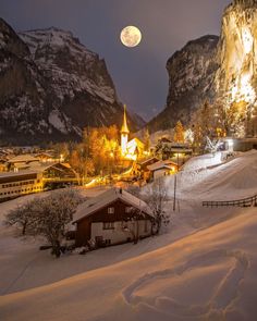 a snowy mountain town with mountains in the background and a full moon rising above it