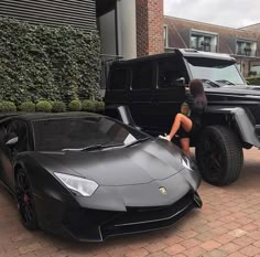 a woman sitting on the hood of a black sports car next to a lambino