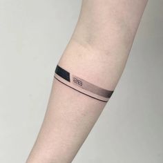 a person with a black and grey wristband tattoo on their left arm that has the letter b in it