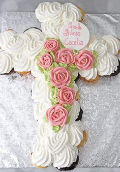 a cross decorated with pink roses and white frosting on top of a cake sheet