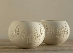 two white vases sitting next to each other on a wooden table with holes in them