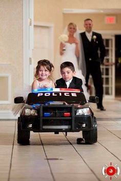 a young boy and girl in a police car on the floor with their wedding party behind them