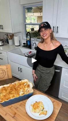 a woman standing in front of a casserole dish on a wooden cutting board