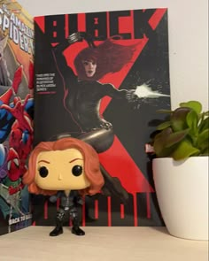 a black widow pop vinyl figure next to a spider - man movie poster on a shelf