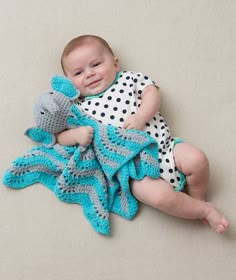 a baby is laying on the floor with a crocheted blanket and holding a stuffed animal