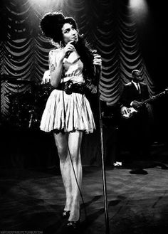 a black and white photo of a woman singing into a microphone while standing on stage