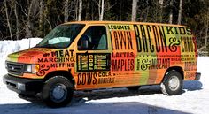 an orange van with words painted on it parked in the snow next to some trees