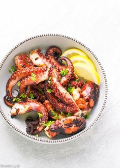 an octopus dish with lemon wedges and parsley in a bowl on a white surface