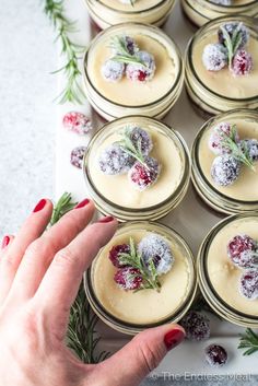 several small jars filled with desserts sitting on top of a white countertop covered in powdered sugar and cranberries