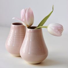 two pink vases with flowers in them on a white tableclothed surface,