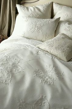 the bed is made with white linens and decorative embroidered sheets, along with pillows