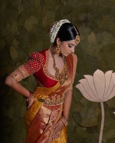 a woman in a red and gold sari standing next to a large white flower