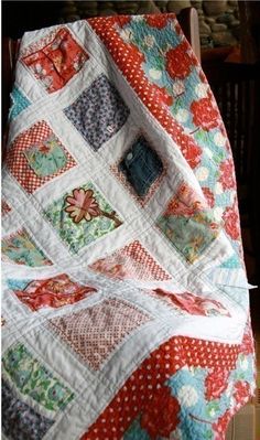 a quilted blanket with red and blue flowers on it, sitting on a chair