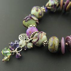 "Like a breath of Spring, you'll love the feel of this handmade lampwork and sterling silver bracelet. The handmade glass beads are combined here with Swarovski crystals and Sterling silver in this one-of-a-kind bracelet. A cluster of Swarovski crystals, and gemstone rondelles including aquamarine and amethyst accents the gorgeous beads in purple, burgundy, celadon, sage and more. A decorative sterling silver butterfly toggle clasp and a dangle of coordinating crystals and gemstones complete the Artisan Czech Glass Beaded Bracelets With Spacer Beads, Lampwork Glass Beads Jewelry, Collage Jewelry, Lampwork Bracelets, Green Board, Purple Burgundy, Glass Bead Bracelet, Fashion Beads, Glass Beads Jewelry