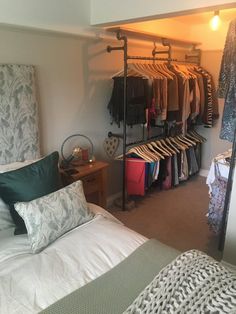 a bed room with a neatly made bed and clothes hanging on the rack next to it