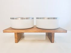 two white bowls sitting on top of a wooden stand