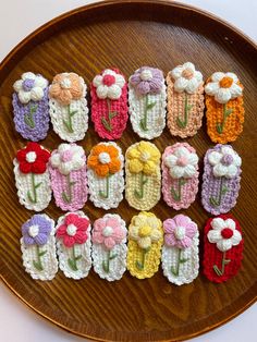 crocheted flowers are arranged in rows on a wooden platter that sits on a table