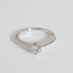 a white gold ring with a single diamond in the center on a plain surface,