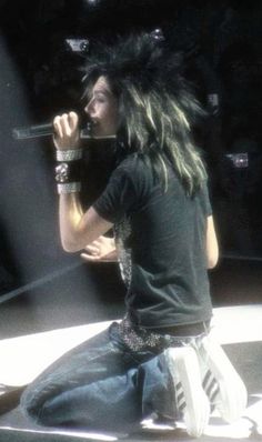 a man with long hair sitting on top of a white floor next to a microphone