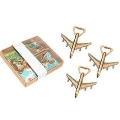 four gold metal airplane clips on top of a card box next to it's contents