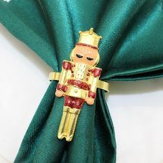 a napkin with a gold and red toy soldier on it's side, sitting on top of a green cloth