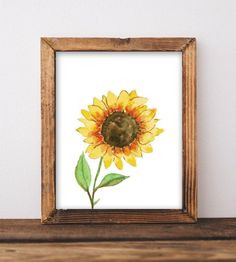 a watercolor painting of a sunflower in a wooden frame on a shelf next to a white wall