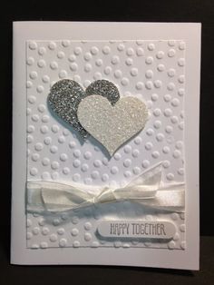 a white card with two hearts and a bow on the front, decorated in silver glitter