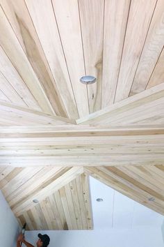 a man is working on the ceiling in his room with wood planks and white walls