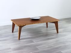 a wooden coffee table with a bowl on it's top, in front of a white wall