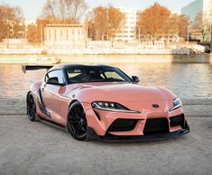 a pink toyota sports car parked next to the water