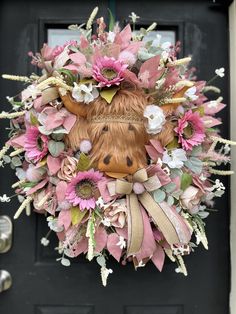 a wreath with a cow's head is hanging on the front door, decorated with pink and white flowers