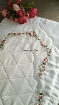 a white table cloth with pink flowers on it and a bouquet of roses in the middle