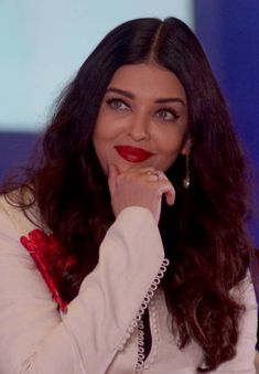 a woman with long dark hair wearing a white shirt and red lipstick is looking at the camera