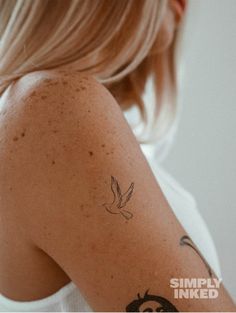 the back of a woman's shoulder with a bird tattoo on her left arm