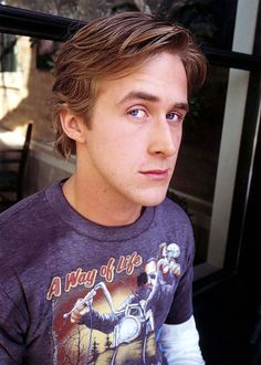 a young man sitting in front of a window with his hand on his hip and looking at the camera