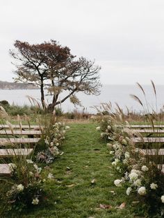 an outdoor ceremony set up with wooden benches and flowers in the foreground, overlooking the ocean