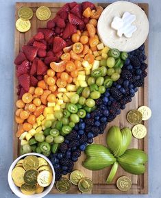 a wooden cutting board topped with lots of fruit next to two bowls of gold coins