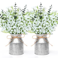 two tin cans filled with white flowers on top of a table next to each other