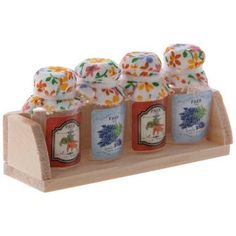 four small jars with flowers on them are sitting in a wooden display holder for soaps