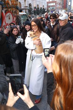 a woman holding a dog in front of a crowd of people taking pictures with their cell phones