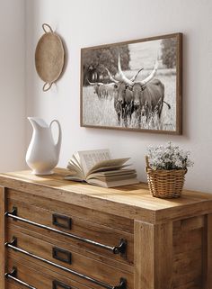 a wooden dresser topped with a book next to a vase filled with flowers and an antelope